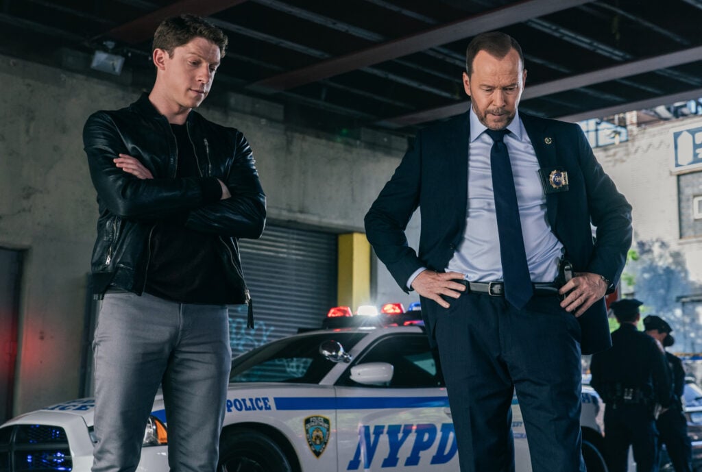 Joe standing with his arms crossed as he and Danny examine evidence at a crime scene on Blue Bloods Season 14 Episode 15