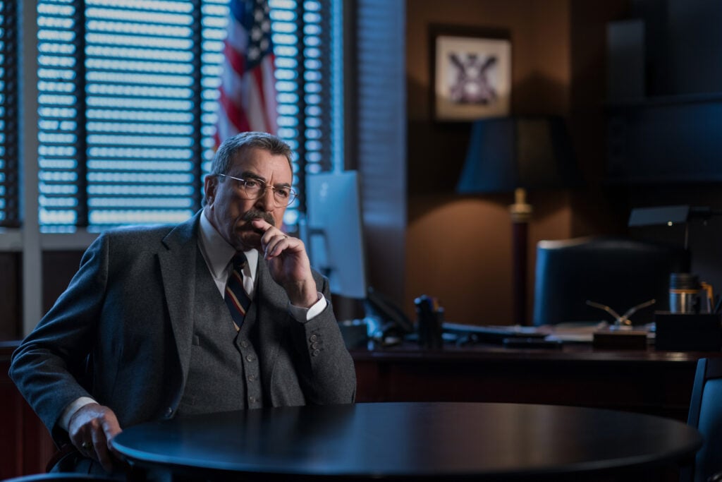 Frank sitting at a table in an office looking thoughtful on Blue Bloods Season 14 Episode 18