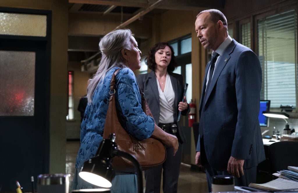 A silver-haired woman approaches Danny in the squad room while Baez watches on Blue Bloods Season 14 Episode 18